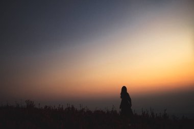 Gün doğmadan önce tepedeki güzel çiçek bahçesinin arasında duran bir kadının silüeti.