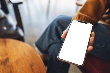 Kafede elinde siyah cep telefonu tutan ve gösteren bir kadının görüntüsü.