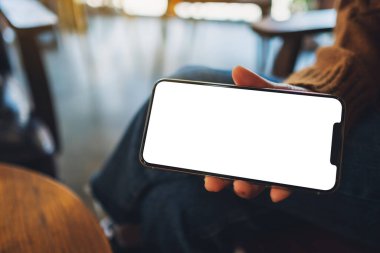 Kafede elinde siyah cep telefonu tutan ve gösteren bir kadının görüntüsü.