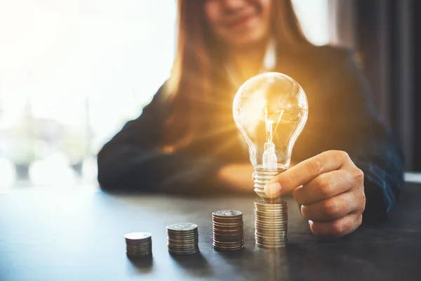 コインの上に電球を保持し 置くビジネスマンは エネルギーとお金の概念を節約するためのテーブルの上に積層 — ストック写真