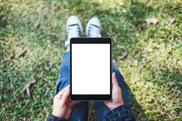 Açık havada otururken boş beyaz masaüstü ekran ile siyah tablet tableti tutan ve kullanan bir kadının en üst görünüm görüntüsü