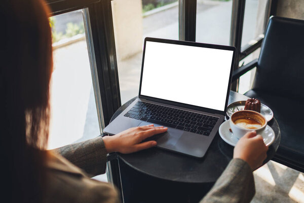 Изображение женщины, использующей и трогающей сенсорную панель ноутбука с чистым белым экраном во время питья кофе в кафе