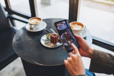 Kafede yemek yemeden önce kahve ve atıştırmalık fotoğraf çeken bir kadın.