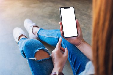 Yerde otururken elinde beyaz ekranlı siyah bir cep telefonu tutan bir kadının görüntüsü.