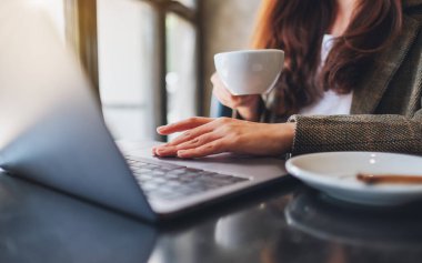 Ofiste kahve içerken laptopta çalışan ve dokunan bir kadının yakın plan görüntüsü.