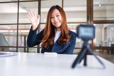 Güzel bir Asyalı kadın blogcu veya vlogger video kaydederken el sallıyor 