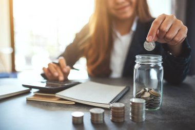 Bir iş kadınının cam kavanoza para istiflediği ve koyduğu yakın plan görüntüsü. 