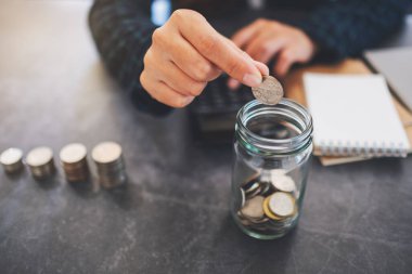 Bir iş kadınının cam kavanoza para istiflediği ve koyduğu yakın plan görüntüsü. 