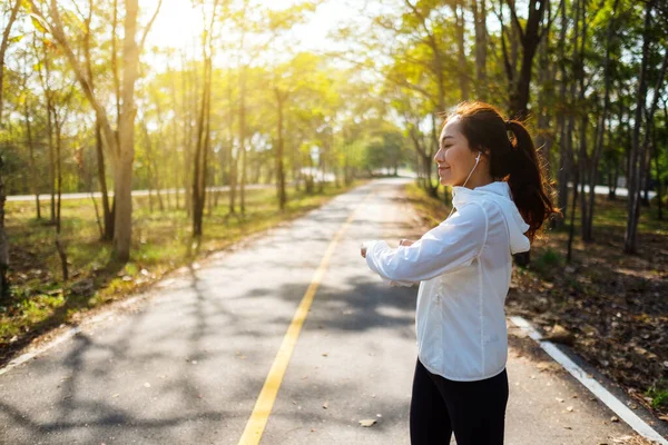 Genç Asyalı bir kadın şehir parkında koşmadan önce kollarını esnetiyor. 