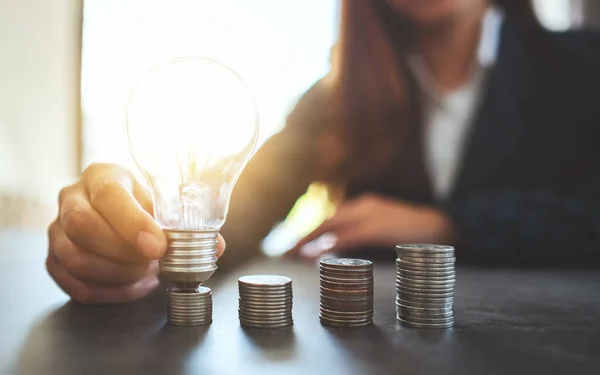 コインの上に電球を保持し 置くビジネスマンは エネルギーとお金の概念を節約するためのテーブルの上に積層 — ストック写真