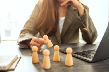 İş kadını lideri ofisteki bir grup çalışanın arasından tahta insanları seçiyor.