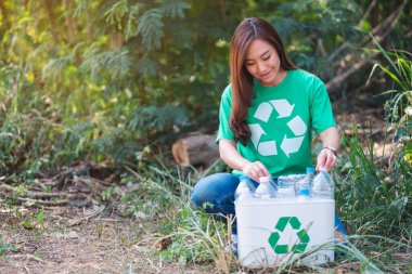 Güzel bir Asyalı kadın eylemci dışarıda çöp kutusuna plastik şişe topluyor.