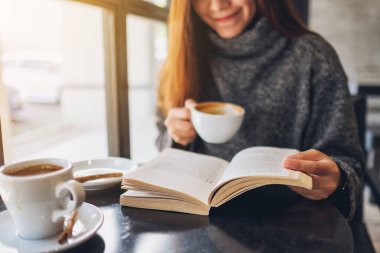 Kafede kahve içerken kitap okuyan güzel bir kadının yakın plan görüntüsü. 