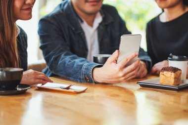 Kafede aynı cep telefonunu kullanan ve ona bakan bir grup Asyalı genç.