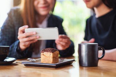 Kadınlar kafede yemeden önce kek ve kahve çekmek için cep telefonu kullanıyor.