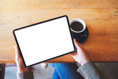 En üstteki görüntüde elinde siyah tablet olan beyaz ekranlı kahve fincanı olan bir kadın resmi var.