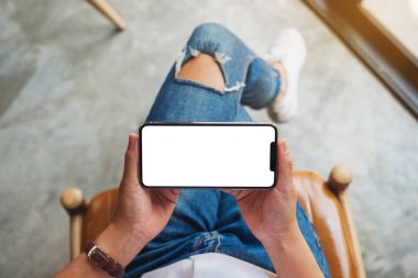 Kafede otururken elinde beyaz ekranlı siyah cep telefonu olan bir kadının üst görünüm görüntüsü