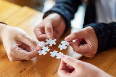 Beyaz yapboz parçalarını bir araya getirip bir araya getiren bir grup insanın yakın plan görüntüsü.