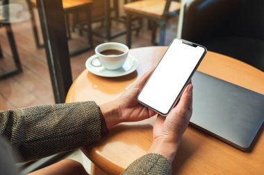 Boş beyaz masaüstü ekranlı, dizüstü bilgisayarı ve kahve fincanı olan bir kadının cep telefonu görüntüsü. 