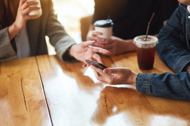 Cep telefonu kullanan ve birlikte kahve içen insanların yakın plan görüntüsü.