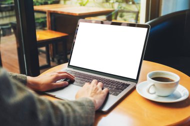 Kafedeki boş beyaz masaüstü ekran ile dizüstü bilgisayarı kullanan ve yazan bir kadının görüntüsü