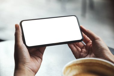 Masasında kahve fincanı olan boş beyaz ekranlı cep telefonu tutan bir kadının görüntüsü.