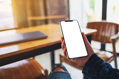 Masasında dizüstü bilgisayarı olan, boş beyaz masaüstü ekranlı cep telefonu tutan bir kadının görüntüsü. 