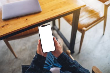 Ofiste otururken elinde boş beyaz ekranla cep telefonu tutan bir kadının üst görünüm görüntüsü