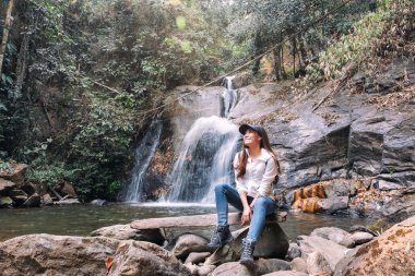 Ormanda şelalenin önünde oturan güzel bir Asyalı kadın.