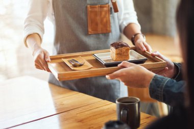 Bir garson, kafede müşteriye bir parça choux kremi ikram ediyor.