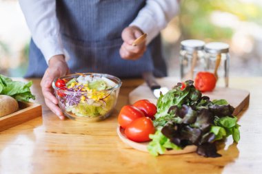 Mutfakta bir kase taze sebze salatası ve yemek pişiren bir kadın şefin yakın plan görüntüsü.