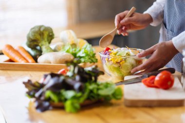 Mutfakta bir kase taze sebze salatası ve yemek pişiren bir kadın şefin yakın plan görüntüsü.