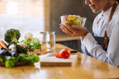 Mutfakta bir kase taze sebze salatası ve yemek pişiren bir kadın şefin yakın plan görüntüsü.
