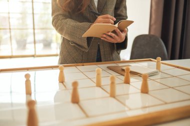 İş kadını lideri, planlama kurulundaki bir grup çalışanın arasından tahta insanları seçerken yazıyor.