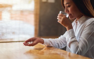 Hasta bir kadının elinde beyaz haplar tutarken, ilaç içerken ve su içerken görüntüsü.