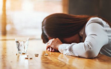 Hasta bir kadının beyaz haplar ve bir bardak suyla masada uyuduğu yakın plan.