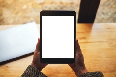 Masada dizüstü bilgisayarlı, boş beyaz masaüstü ekranlı, elinde siyah tablet bilgisayar tutan bir kadının en üstteki görüntüsü 