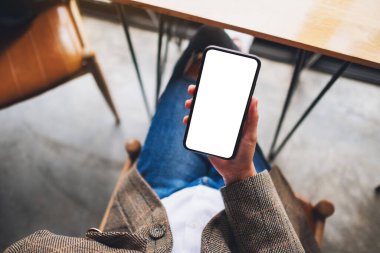 Ofiste otururken elinde boş beyaz ekranla cep telefonu tutan bir kadının üst görünüm görüntüsü