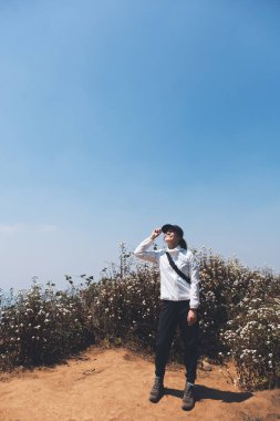 Mavi arka planda dağların tepesinde yürüyüş yapan ve ayakta duran bir kadın.