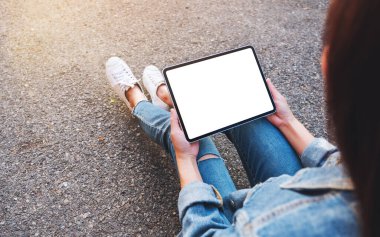 Açık havada otururken elinde boş beyaz tabletle siyah bir tablet tutan bir kadının görüntüsü. 