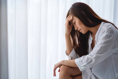 Üzgün ve stresli Asyalı bir kadın yatak odasında yalnız oturuyor.