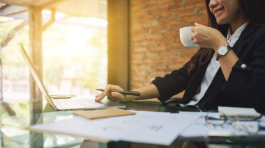 İş kadını ofiste kahve içerken dizüstü bilgisayar kullanıyor.