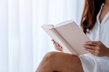 Evdeki bir yatak odasında kitap okuyan Asyalı güzel bir kadının yakın çekimi.