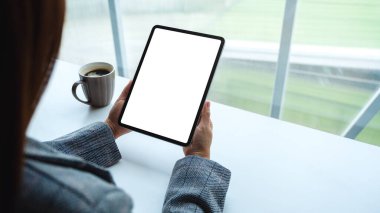 Masasında kahve fincanı olan siyah tabletli beyaz ekranlı bir kadının görüntüsü.