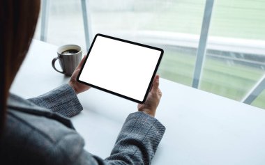 Masasında kahve fincanı olan siyah tabletli beyaz ekranlı bir kadının görüntüsü.