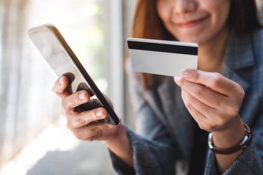 Güzel bir Asyalı kadın cep telefonundan alışveriş yapmak için kredi kartı kullanıyor.