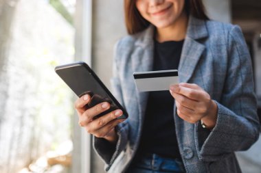 Güzel bir Asyalı kadın cep telefonundan alışveriş yapmak için kredi kartı kullanıyor.