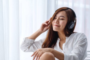Güzel bir Asyalı kadın, yatak odasında kulaklıkla müzik dinlemekten, mutluluk ve rahatlama kavramlarından hoşlanır.
