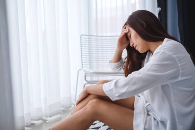 Üzgün ve stresli Asyalı bir kadın yatak odasında yalnız oturuyor.