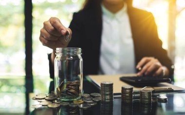 Cam kavanoza bozuk para koyan, tasarruf ve finansal konsept için para biriktiren bir iş kadınının yakın plan görüntüsü.